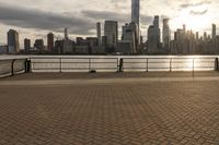 a person on the boardwalk near a fence overlooking a river and city skyline at sunset