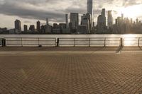 a person on the boardwalk near a fence overlooking a river and city skyline at sunset