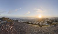 a view looking down at the road from a hill overlooking a city below, at sunset