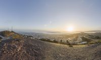 a view looking down at the road from a hill overlooking a city below, at sunset