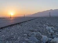 a paved road that runs through a rocky area and sunset with power poles in the distance