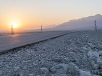 a paved road that runs through a rocky area and sunset with power poles in the distance