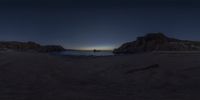 the sun sets on an empty beach with waves crashing toward the rocks, with two small boats out on the water