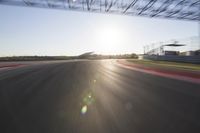 the sun is setting on a race track with a blurry view of a man's car and motorcycle in the motion