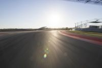 the sun is setting on a race track with a blurry view of a man's car and motorcycle in the motion