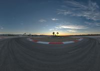 a race track surrounded by palm trees with sun setting in the back ground of it