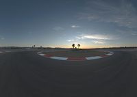 a race track surrounded by palm trees with sun setting in the back ground of it