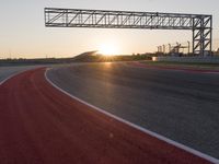 the sun sets behind a driving track near the road course of a racetrack with a few cars driving under it