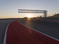 the sun sets behind a driving track near the road course of a racetrack with a few cars driving under it