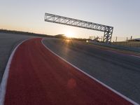 the sun sets behind a driving track near the road course of a racetrack with a few cars driving under it