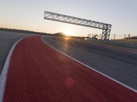 the sun sets behind a driving track near the road course of a racetrack with a few cars driving under it