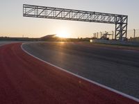 the sun sets behind a driving track near the road course of a racetrack with a few cars driving under it