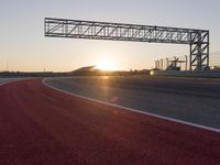 the sun sets behind a driving track near the road course of a racetrack with a few cars driving under it