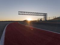 the sun sets behind a driving track near the road course of a racetrack with a few cars driving under it