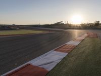 the setting sun casts its rays on a race track with the grass in between the track lanes