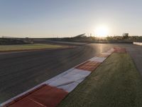 the setting sun casts its rays on a race track with the grass in between the track lanes