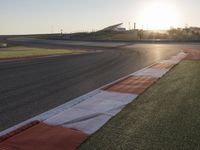 the setting sun casts its rays on a race track with the grass in between the track lanes