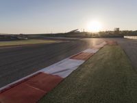 the setting sun casts its rays on a race track with the grass in between the track lanes