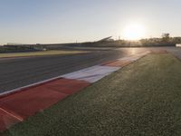 the setting sun casts its rays on a race track with the grass in between the track lanes