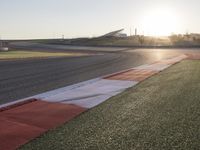 the setting sun casts its rays on a race track with the grass in between the track lanes