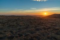 the sunset is reflecting off the mountain range above the grass field on a hill that looks like a hillside