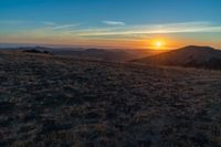 the sunset is reflecting off the mountain range above the grass field on a hill that looks like a hillside