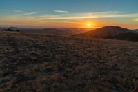 the sunset is reflecting off the mountain range above the grass field on a hill that looks like a hillside