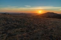 the sunset is reflecting off the mountain range above the grass field on a hill that looks like a hillside