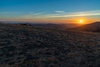 the sunset is reflecting off the mountain range above the grass field on a hill that looks like a hillside