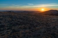 the sunset is reflecting off the mountain range above the grass field on a hill that looks like a hillside