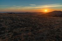 the sunset is reflecting off the mountain range above the grass field on a hill that looks like a hillside