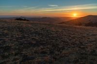 the sunset is reflecting off the mountain range above the grass field on a hill that looks like a hillside