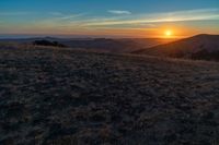 the sunset is reflecting off the mountain range above the grass field on a hill that looks like a hillside