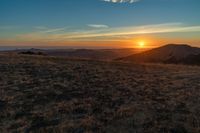 the sunset is reflecting off the mountain range above the grass field on a hill that looks like a hillside