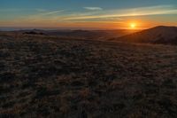 the sunset is reflecting off the mountain range above the grass field on a hill that looks like a hillside