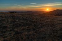 the sunset is reflecting off the mountain range above the grass field on a hill that looks like a hillside