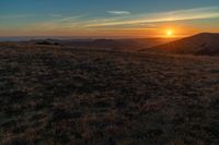 the sunset is reflecting off the mountain range above the grass field on a hill that looks like a hillside