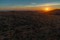 the sunset is reflecting off the mountain range above the grass field on a hill that looks like a hillside