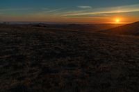 the sunset is reflecting off the mountain range above the grass field on a hill that looks like a hillside