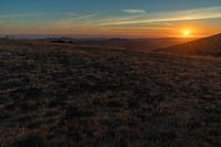 the sunset is reflecting off the mountain range above the grass field on a hill that looks like a hillside