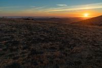 the sunset is reflecting off the mountain range above the grass field on a hill that looks like a hillside