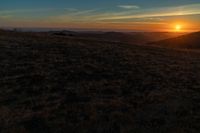 the sunset is reflecting off the mountain range above the grass field on a hill that looks like a hillside