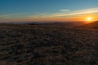 the sunset is reflecting off the mountain range above the grass field on a hill that looks like a hillside