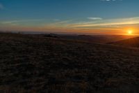 the sunset is reflecting off the mountain range above the grass field on a hill that looks like a hillside