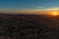 the sunset is reflecting off the mountain range above the grass field on a hill that looks like a hillside