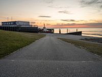 a paved path leading to a seafront next to a body of water at sunset