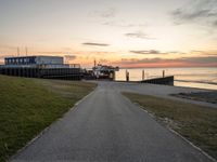 a paved path leading to a seafront next to a body of water at sunset