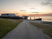 a paved path leading to a seafront next to a body of water at sunset