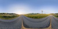 three lane asphalt road with two windmill in the distance on sunset day with grass on ground and mountains in background