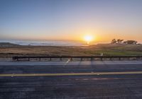 a beautiful sunset on the road by the ocean on a clear day with only one car in sight